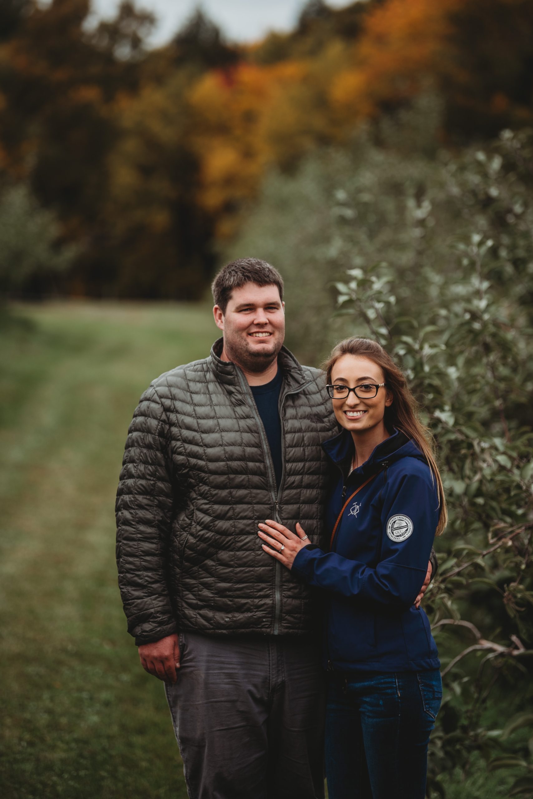 Young couple smiling after a surprise proposal in a apple orchard in Maine